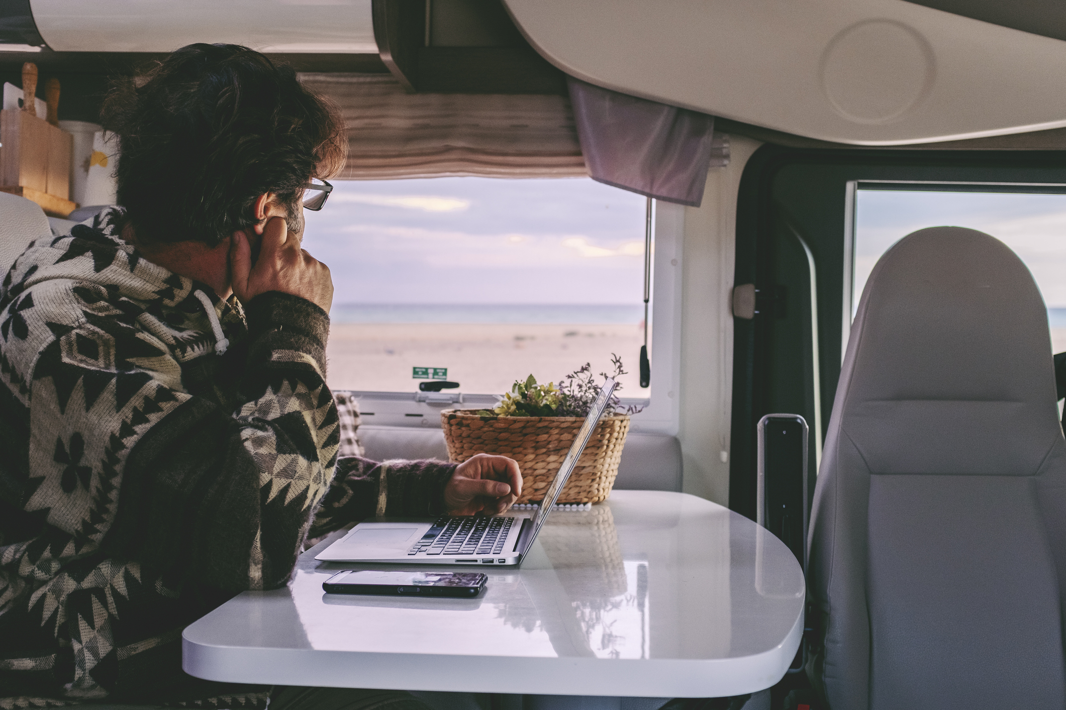 Person sitting at a table in an RV looking out the window with a laptop on the table
